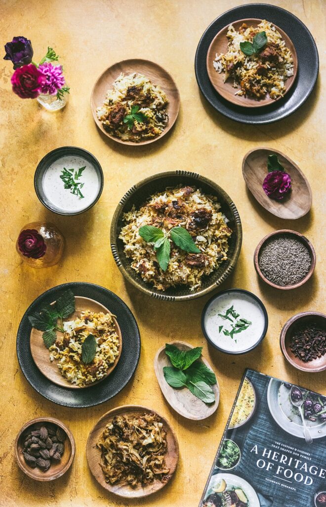 Plate and platters of Hyderabadi Mutton Biryani on gold backdrop.