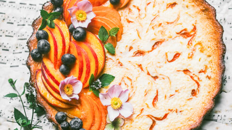 creamy apricot tart swirled with jam and covered with decorative arrangement of apricots, nectarines, blueberries, anemoies, and mint