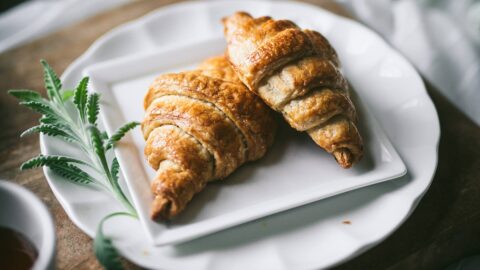 homemade croissants sit on elegant white plates over wooden cutting board in fresh breakfast in bed scene