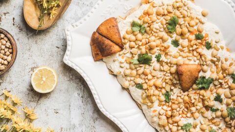 light and bright photo of warm chickpea cassrole topped with pita chips pine nuts and parsley