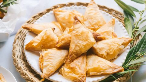 plate of golden crispy tiropitas on grecian scene with olive greenery