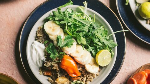 plate of somalian isku dhex karis garnished with bananas, greens, and bright orange chili peppers
