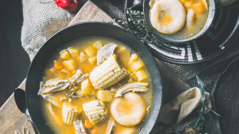 dumplings float in golden bowl of jamaican chicken soup along with corn and other vegetables