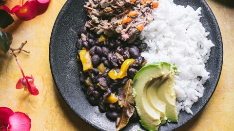 venezuelan white rice black beans and shredded skirt steak make up a plate of pabellion criollo. garnished with avocado.