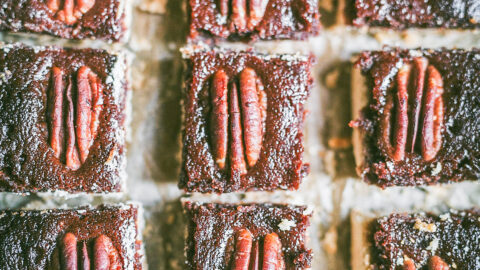 small shortbread pecan date bars cut exactly the size of the pecans nestled into each. lined up on brown butcher paper