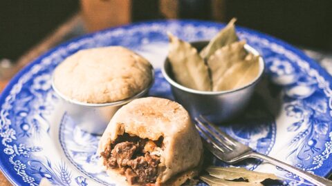 2 individual steak and kidney puddings sit on a blue plate with bite taken out of one showing steak and gravy