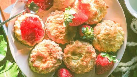 Devon lemon strawberry jam drips out of a classic English scone garnished with whole strawberries