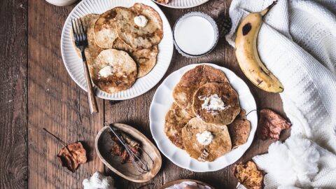 overhead shot of plates of banana omelette surrounded by brown eggs, whole bananas, sliced bananas, creamy cozy white blanket, and more autumn styling