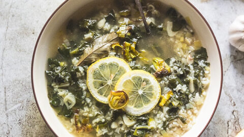 overhead shot of heathy green garlic soup (sopa de ajo) full of spinach and leeks and garnished with lemons and crispy fried leeks