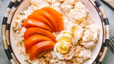 perfect square overhead shot of best potato salad garnished w fresh tomato wedges, hard boiled eggs, and smoked paprika