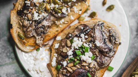 two perfectly golden slices of sourdough toast topped with mushrooms, gravy, and loads of healthy toppings