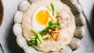 Square image of Thai Jok topped with half a boiled egg, spring onion, cilantro, and crispy onions